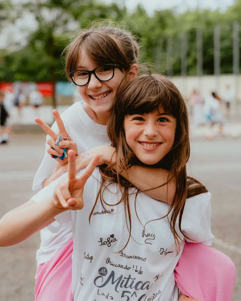Due bambine sorridenti con il segno di vittoria in cortile