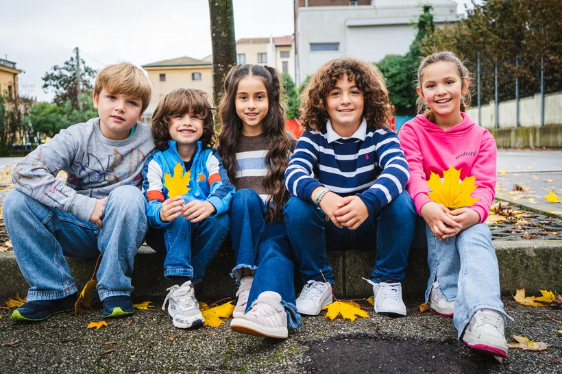 Cinque bambini della primaria seduti sul gradino in cortile, con le foglie d’autunno