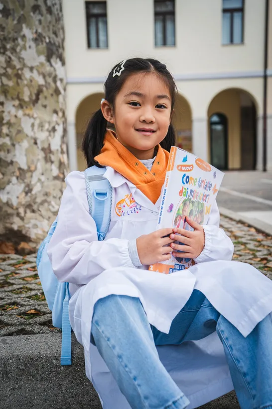 Bambina della primaria con il grembiule e un libro in mano